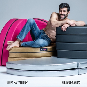 Vari Tappetini di Sicurezza Lupit Pole impilati, con Alberto del Campo seduto su di essi, indossando solo dei jeans.